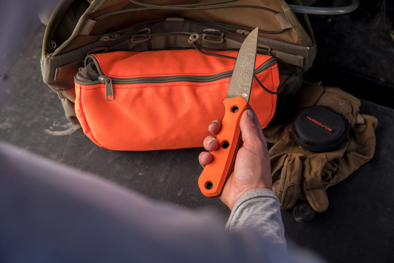 Person holding a knife with an orange handle over an open orange bag.
